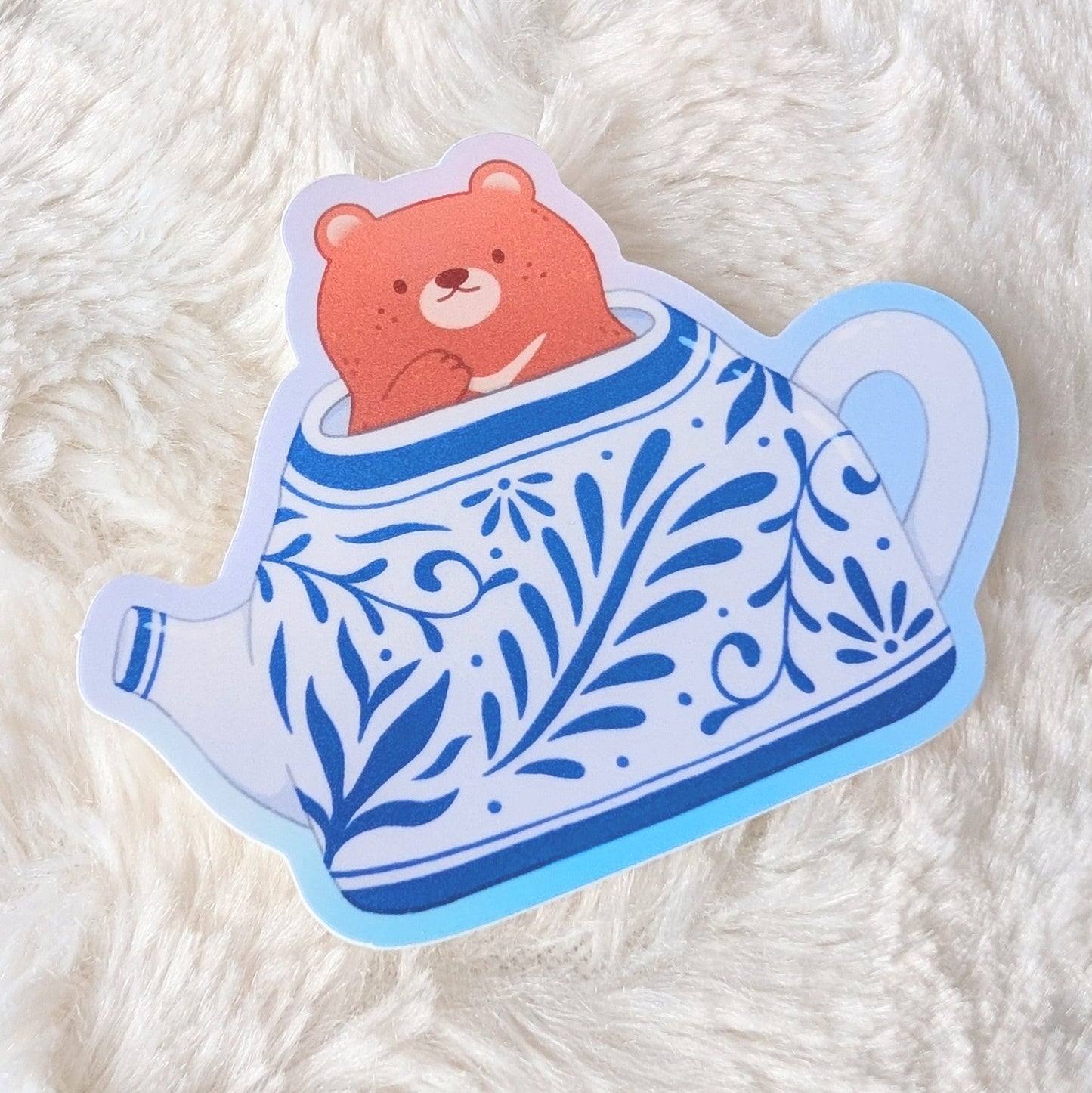 Sticker of a bear in a teapot on a white fluffy surface