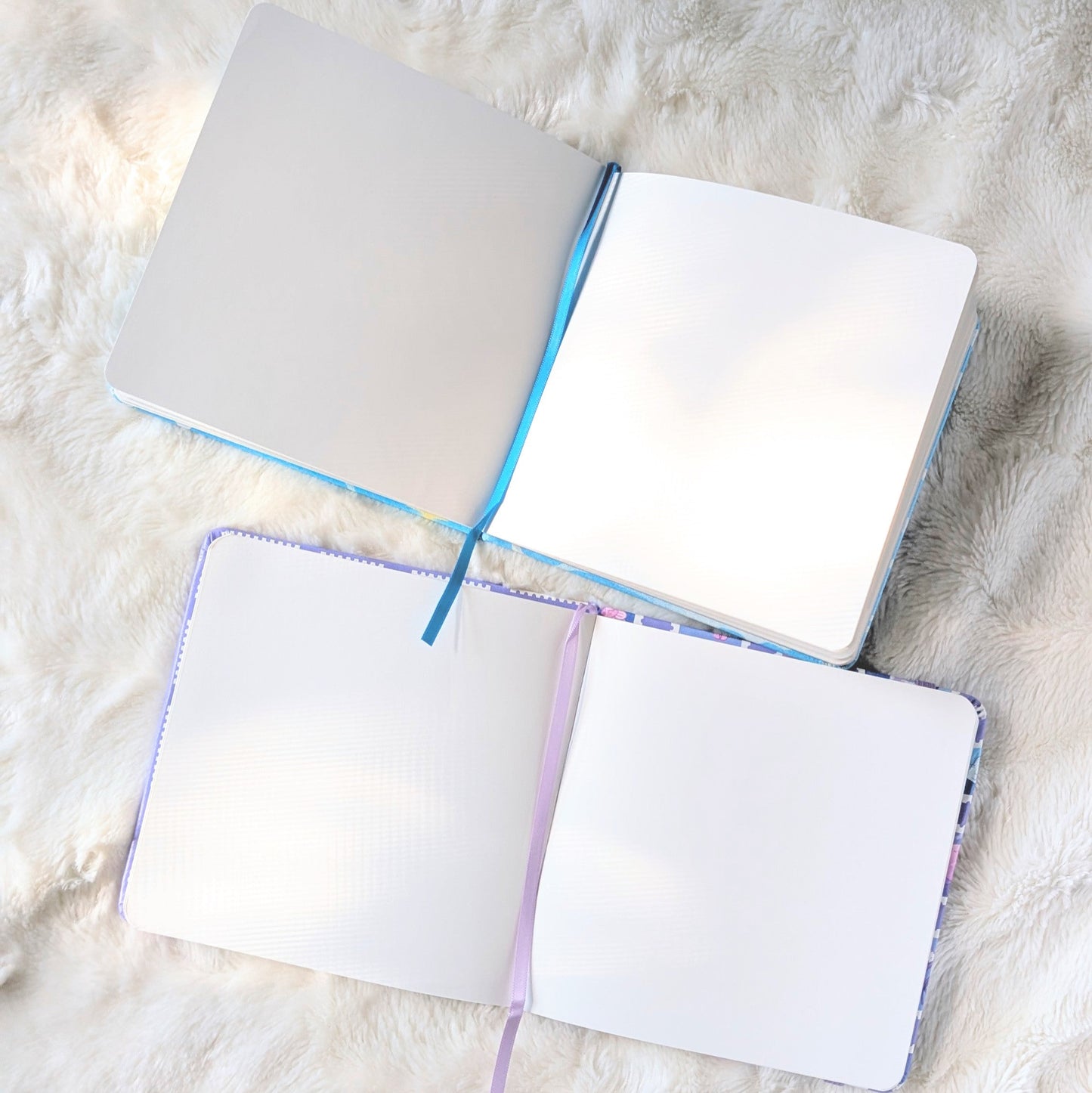 Two open sketchbooks with colorful edges on a textured white surface