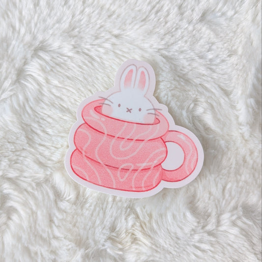 Sticker of a rabbit in a pink cup on a fluffy white surface