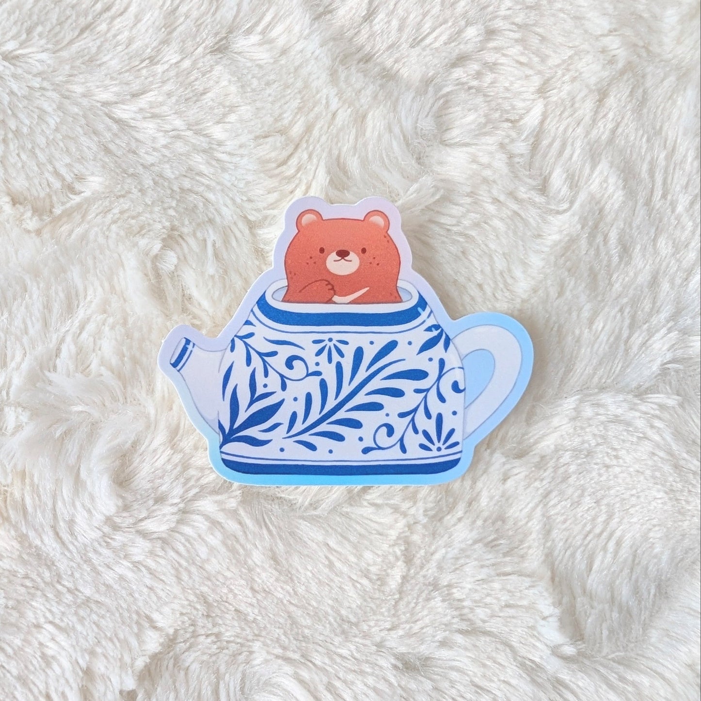 Sticker of a bear in a teapot on a textured white surface