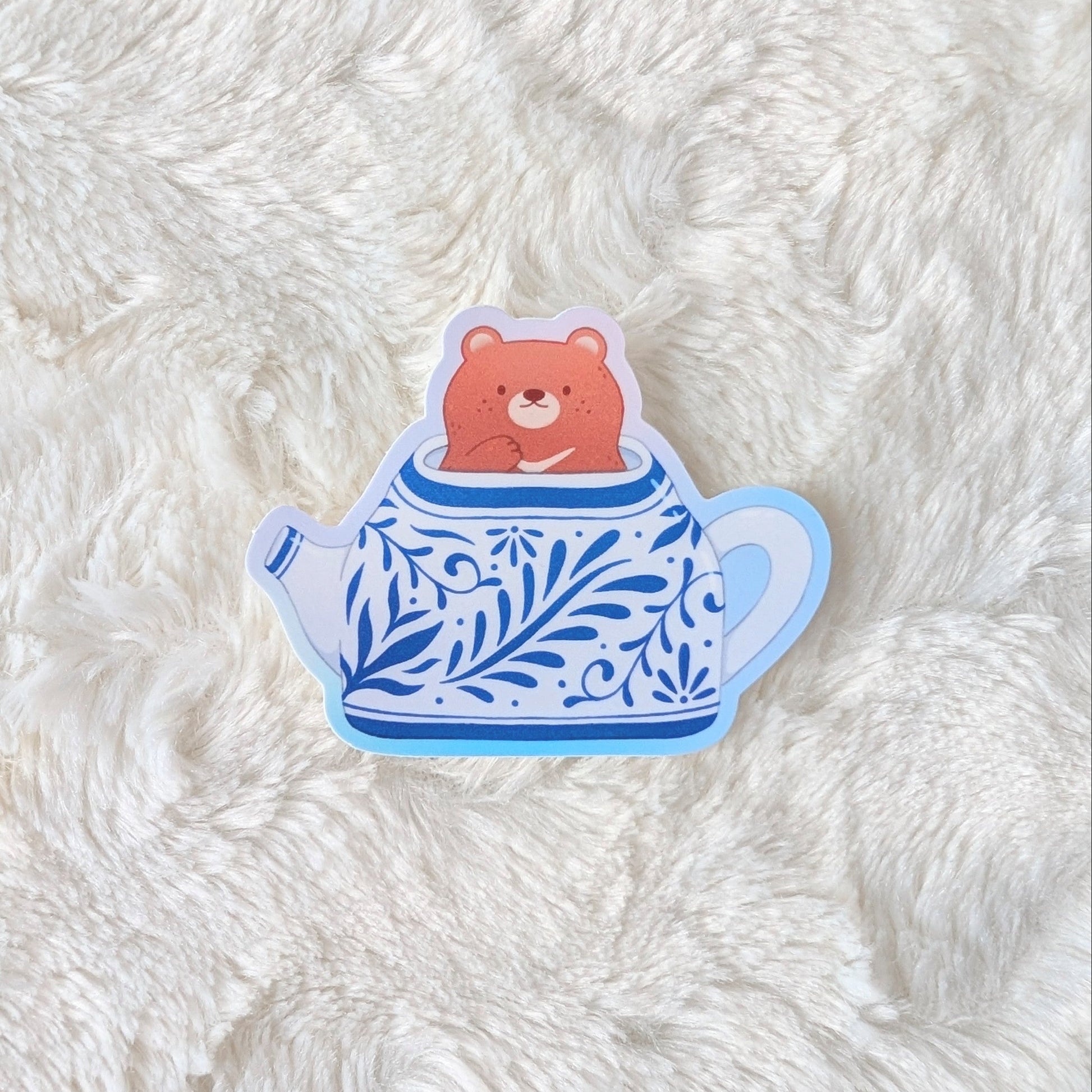 Sticker of a bear in a teapot on a textured white surface