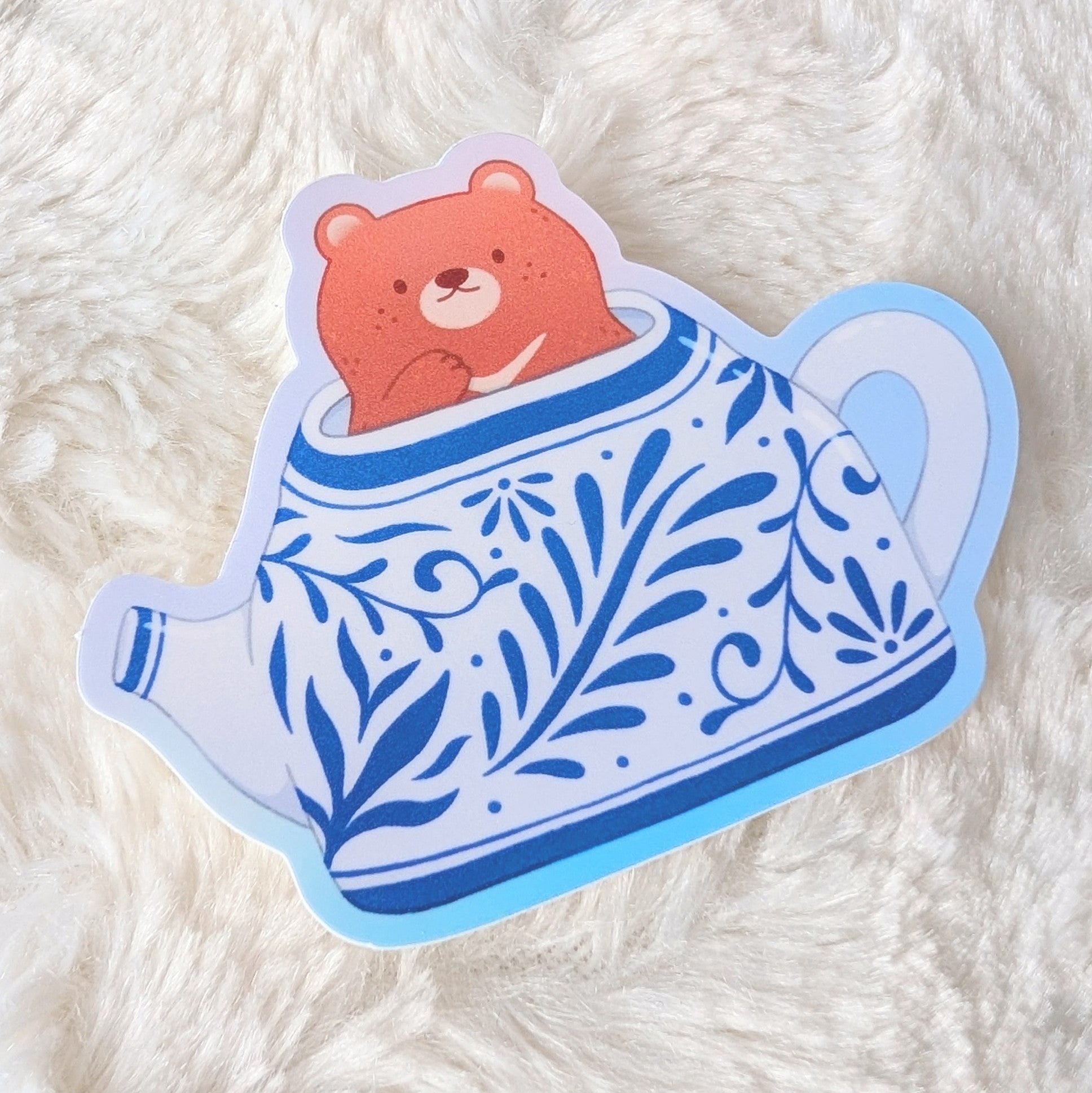 Sticker of a bear in a teapot on a white fluffy surface