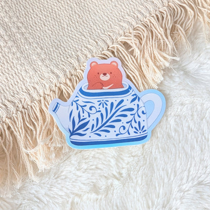 Sticker of a bear in a teapot on a textured fabric background