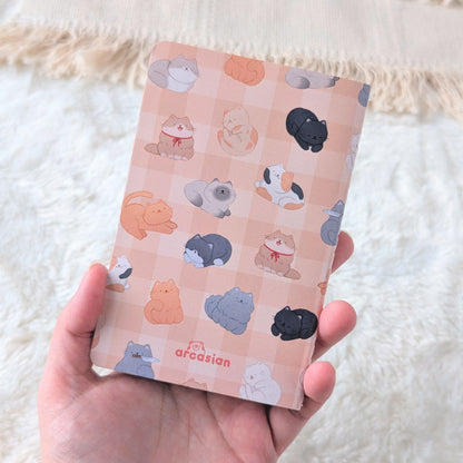 Hand holding a small notebook with cat illustrations on a white textured background