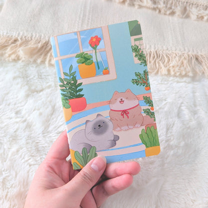 Hand holding a colorful card with a cat and plant design on a textured fabric background