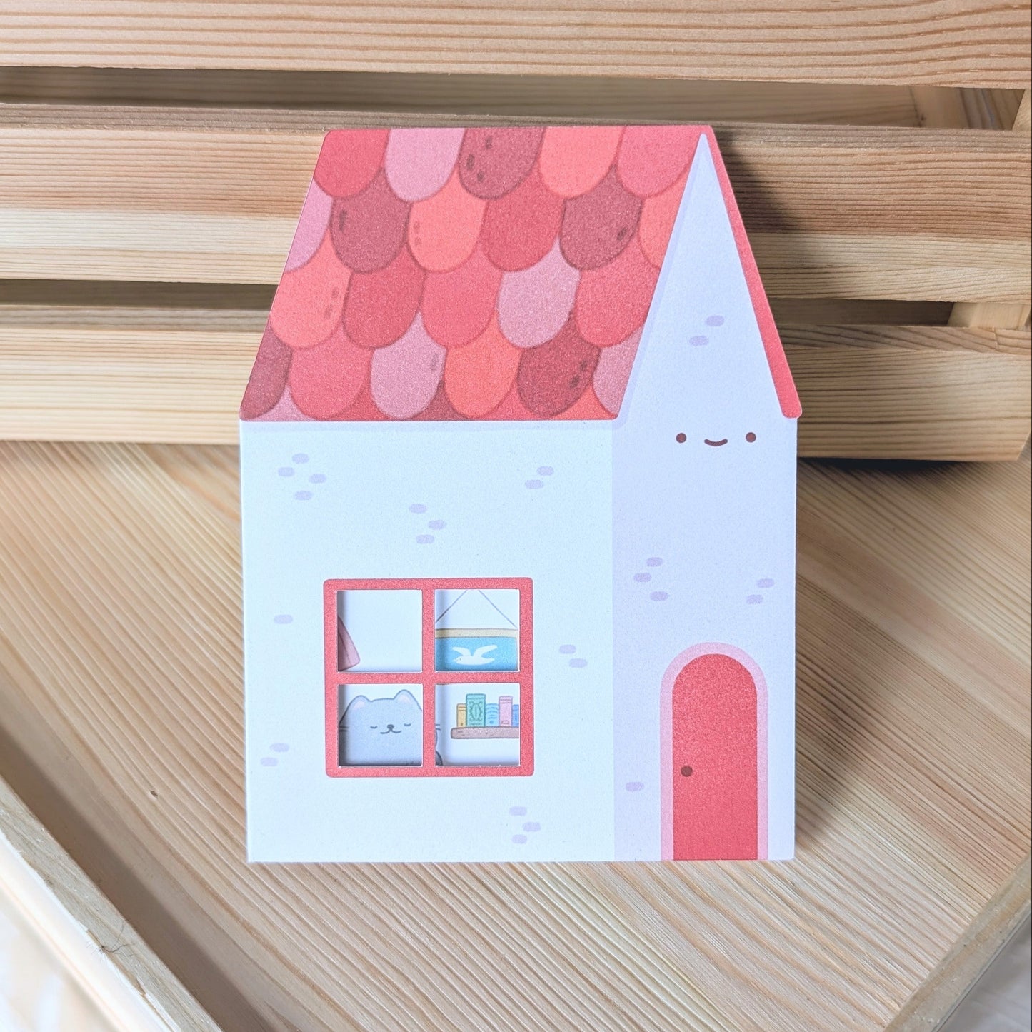 Small house-shaped card with a red roof and white body on a wooden surface