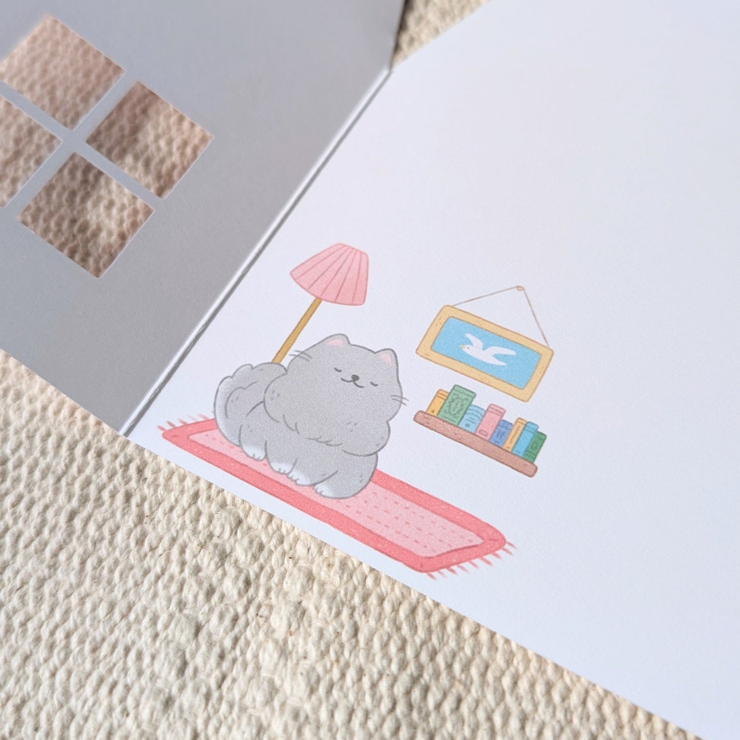 Card with a cute illustration of a cat on a rug, placed on a textured surface.