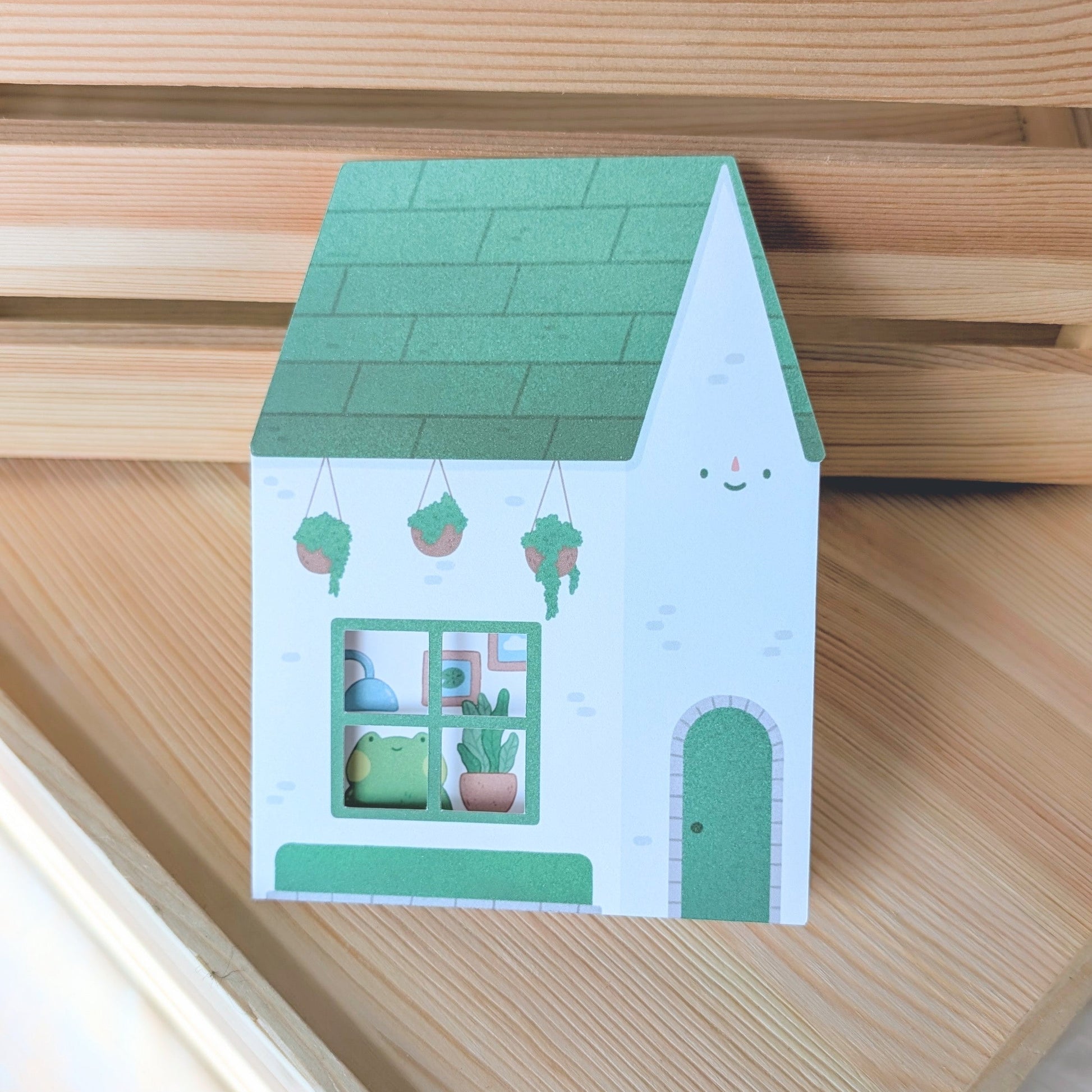 Small paper house model with green roof and windows on a wooden surface