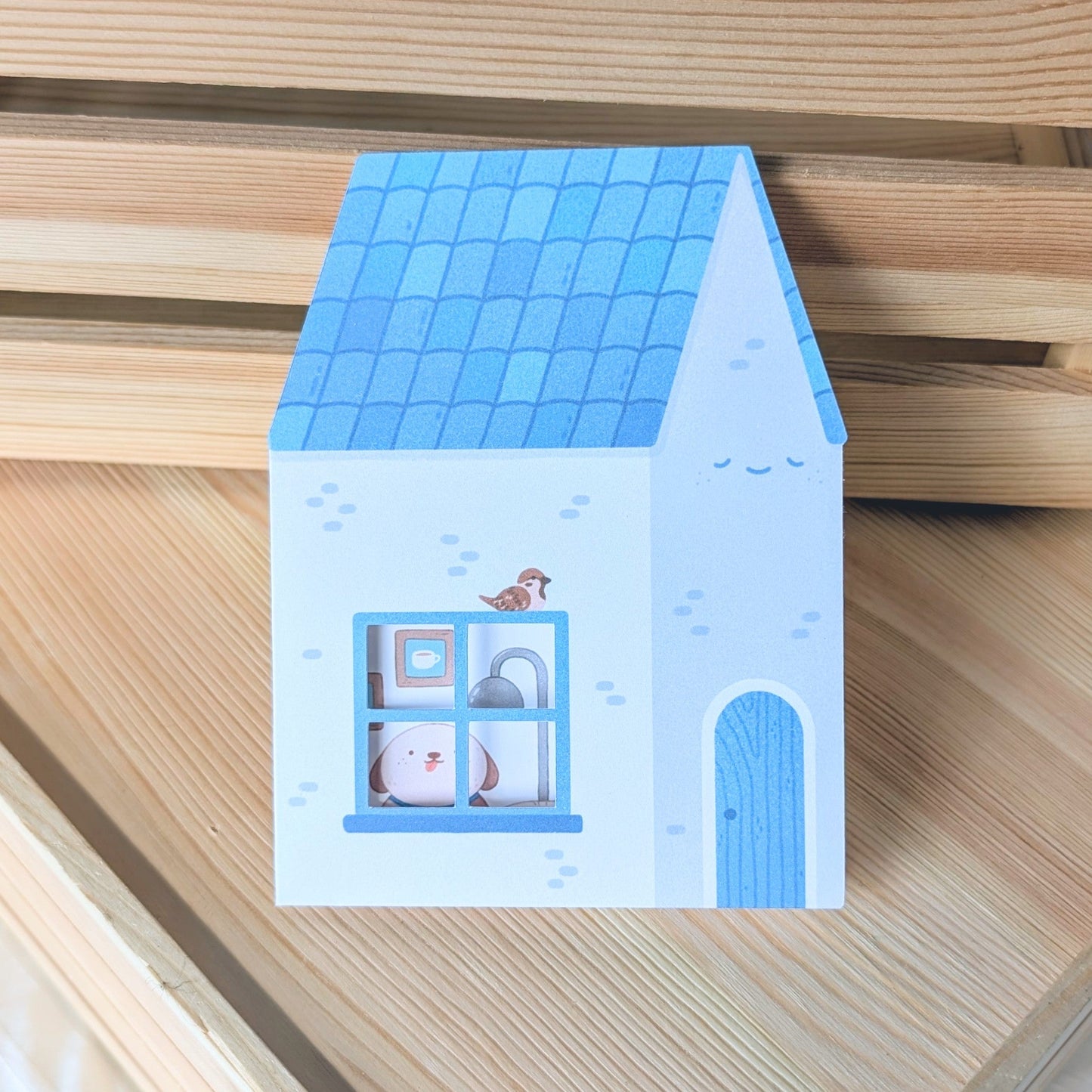 Small house-shaped card with a blue roof and window on a wooden surface