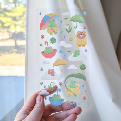 Hand holding a sheet of colorful stickers with cartoon characters against a white curtain.