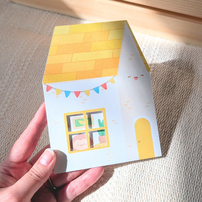 Hand holding a small card with a house design on a textured surface
