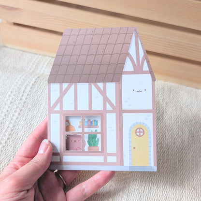 Small house-shaped card held by a hand on a textured surface