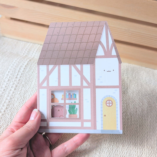 Small house-shaped card held by a hand on a textured surface