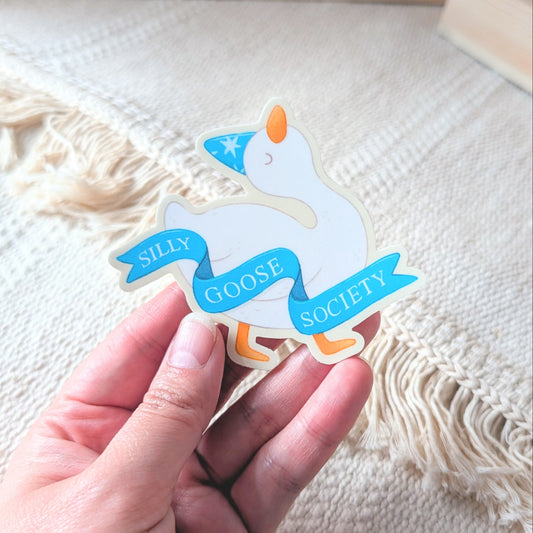 Hand holding a sticker with a goose design on a textured surface