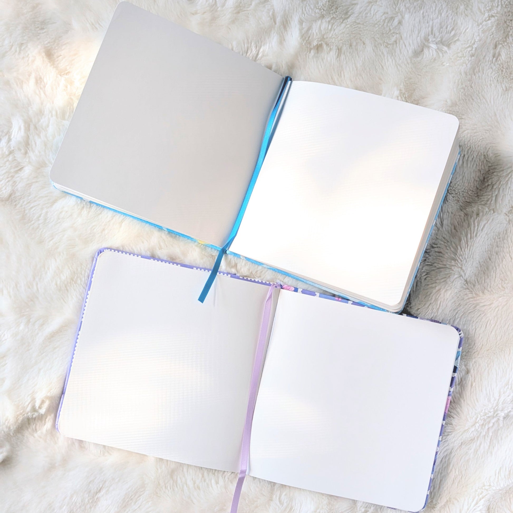 Two open sketchbooks with colorful edges on a textured white surface