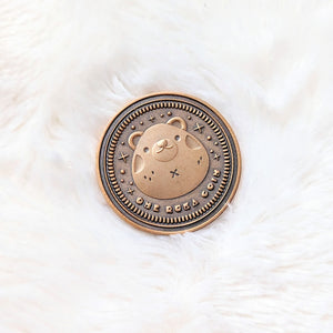 A photo of the front side of a coin made from zinc alloy with an antique gold finish. The coin features a bear in the middle and sparkle details around it. Under the bear it reads "One Ruka Coin".