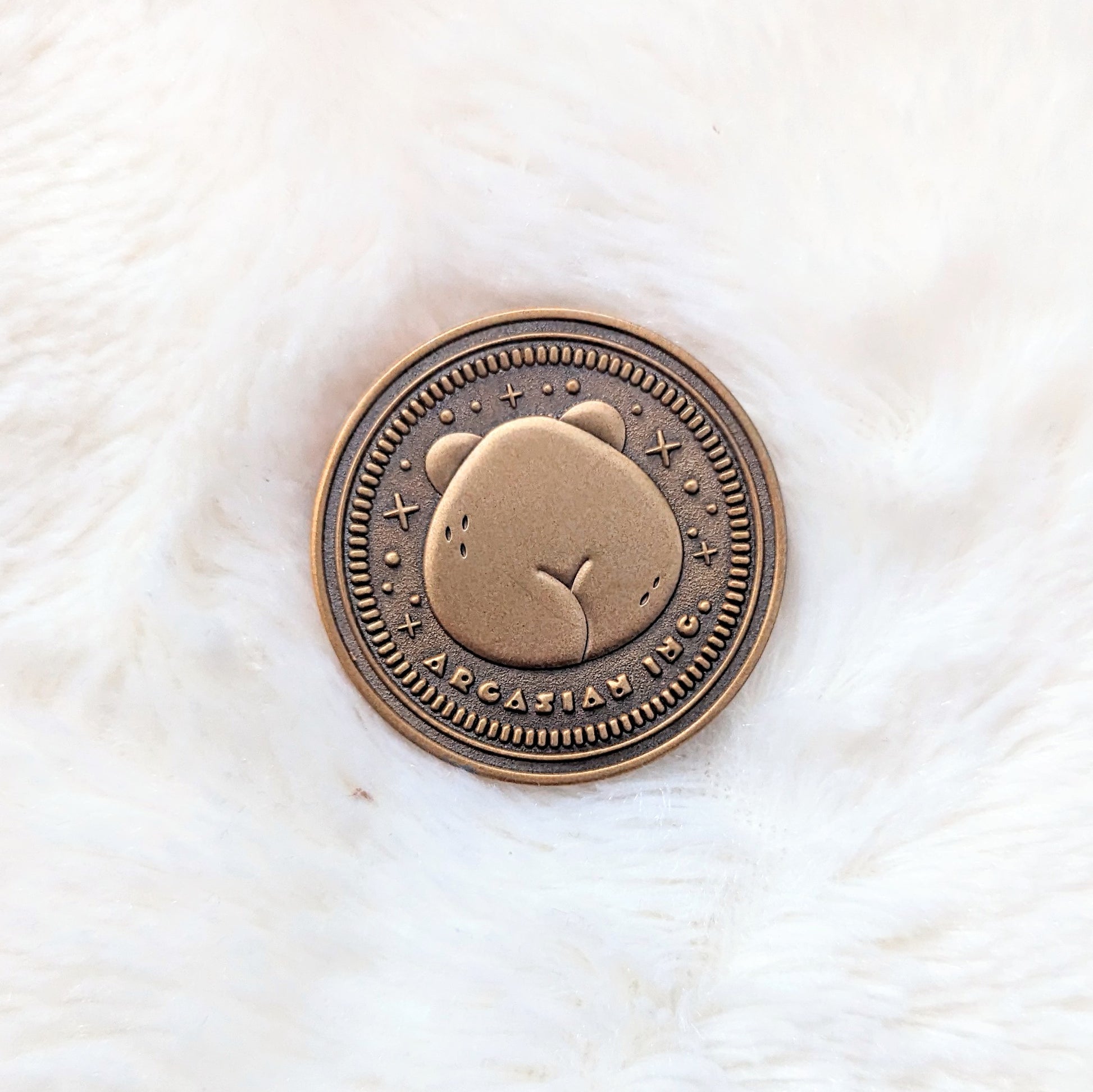 A photo of the backside of a zinc alloy coin with an antique gold finish. The design features the backside of a bear including a cute butt crack and text under the bear that reads "Arcasian Inc."